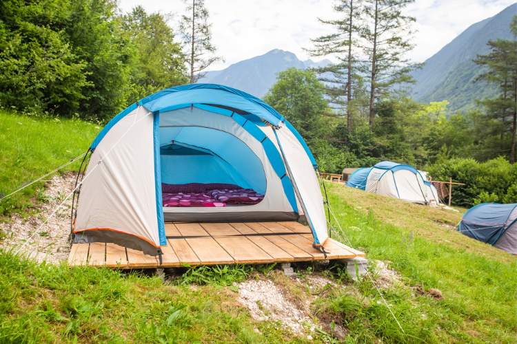Tienda de campana azul y gris abierta en un camping rodeada de montanas